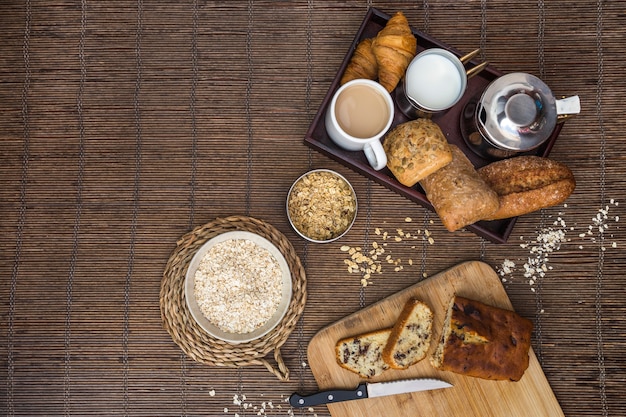 Vista elevada de alimentos horneados, té, leche y avena en mantel individuales