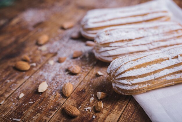 Una vista elevada de almendras con hileras de eclairs horneados en el escritorio de madera