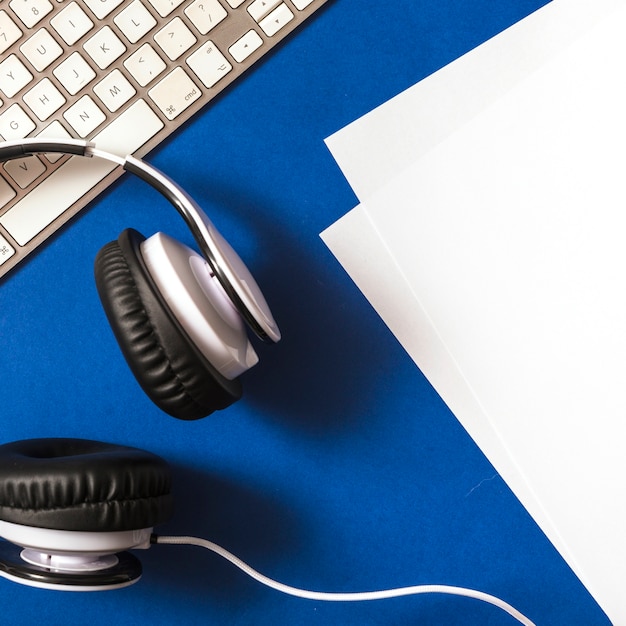 Vista elevada de los auriculares; papel y teclado sobre fondo azul