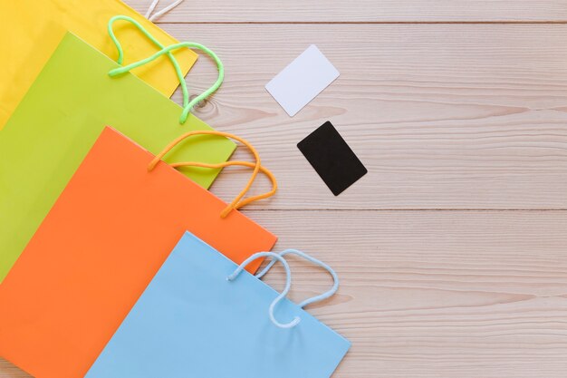 Vista elevada de los bolsos de compras coloreados multi con la tarjeta en blanco en el escritorio de madera