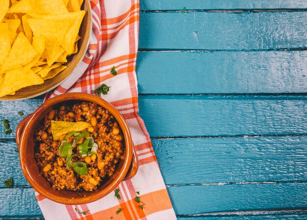 Vista elevada de carne molida cocida en un tazón con nachos mexicanos fritas en el escritorio de madera azul