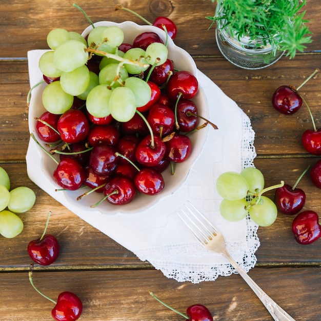 Vista elevada de cerezas y uvas en un tazón en tablón de madera