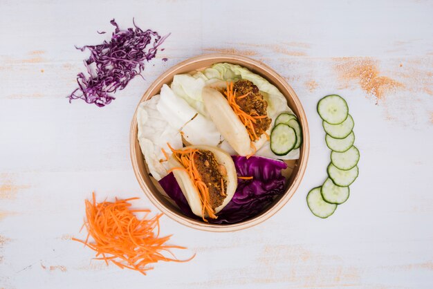 Una vista elevada de la comida tradicional taiwan gua bao en vapor con ensalada sobre fondo de textura de madera