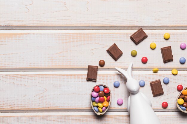 Una vista elevada del conejito blanco con caramelos de gemas y trozos de chocolate en un tablón de madera