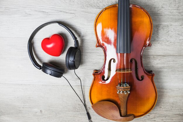 Vista elevada del corazón rojo rodeado de auriculares y guitarra clásica de madera en la mesa gris