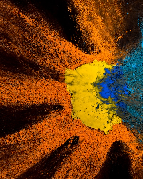 Foto gratuita vista elevada del diseño de polvo holi amarillo, naranja y azul sobre fondo negro