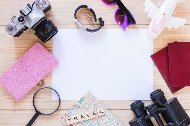 Vista elevada de diversos equipos de viaje y papel blanco en blanco sobre fondo de madera