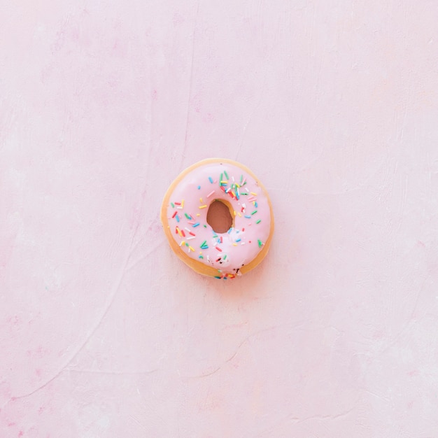 Vista elevada de donut con chispas sobre fondo rosa