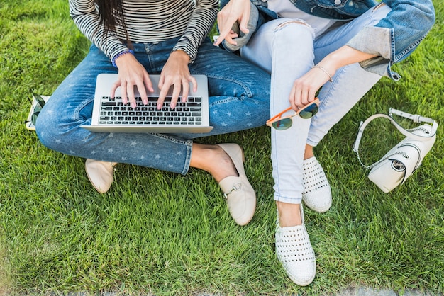 Foto gratuita vista elevada de dos mujeres sentadas en la hierba verde usando una computadora portátil