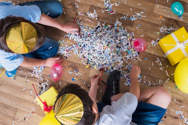 Vista elevada de dos niños reuniendo confeti en piso de madera