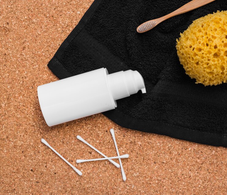 Foto gratuito vista elevada de esponja de baño; cepillo de dientes; toalla; cosmética botella y hisopo de algodón sobre fondo de corcho