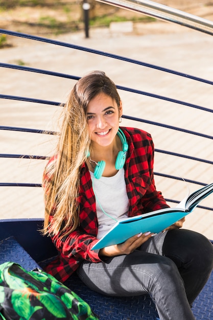 Una vista elevada del estudiante universitario sentado en la escalera sosteniendo un libro en la mano