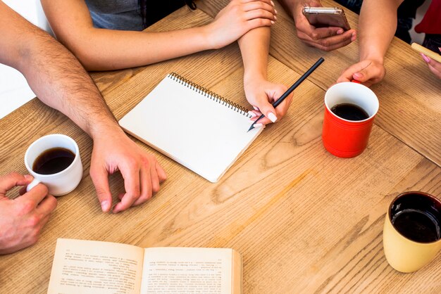 Vista elevada de estudiantes con materiales de estudio y tazas de café en una mesa con textura de madera