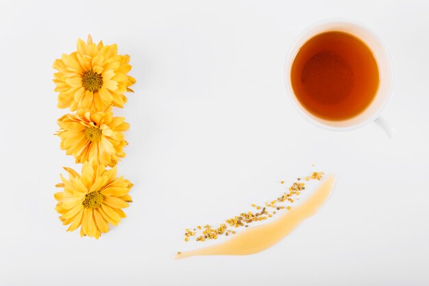 Vista elevada de flores; miel; polen de abeja y té en superficie blanca