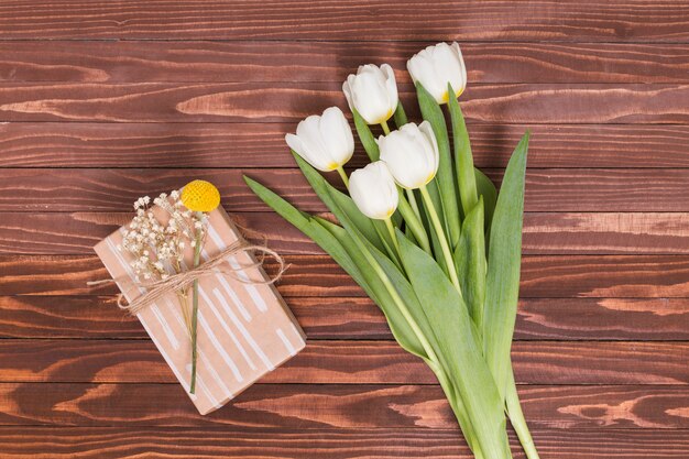 Vista elevada de flores de tulipán blanco con caja de regalo sobre fondo con textura de madera