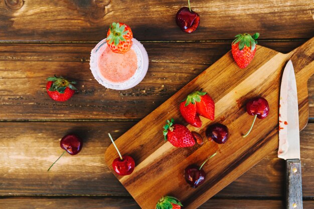 Vista elevada de fresas; cerezas y cuchillo en la tabla de cortar