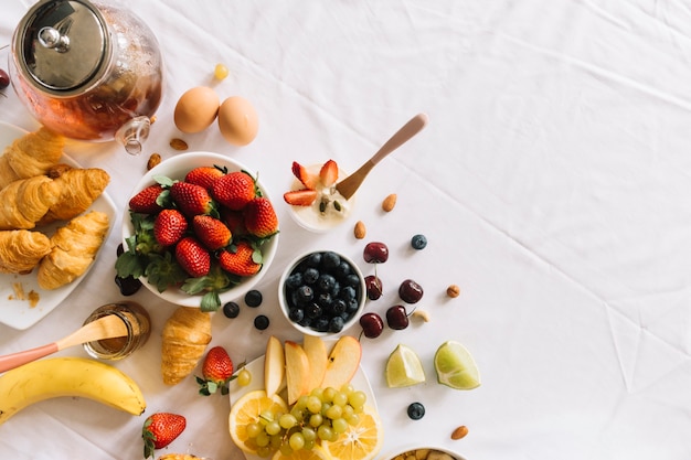 Vista elevada de frutas frescas; yogur; Huevo y croissant sobre fondo blanco