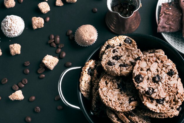 Una vista elevada de galletas en utensilios y granos de café sobre fondo negro