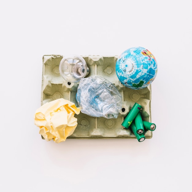 Foto gratuita vista elevada del globo, bombilla, papel arrugado, botella de plástico y pilas en cartón de huevos