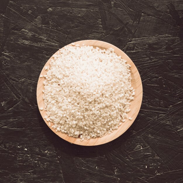 Vista elevada de granos de arroz crudo en un tazón sobre fondo gris áspero