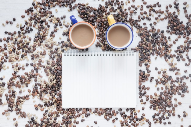 Foto gratuita vista elevada de los granos de café y la taza de café con libro espiral en blanco