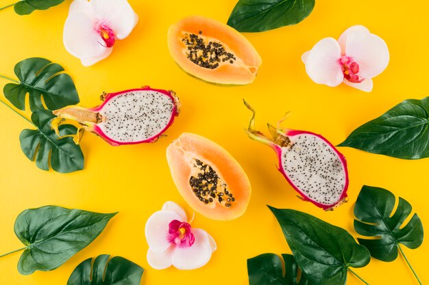 Una vista elevada de hojas artificiales con flor de orquídea; Dragón a la mitad y papaya sobre fondo amarillo