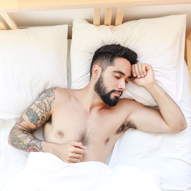 Vista elevada de un hombre sin camisa durmiendo en la cama