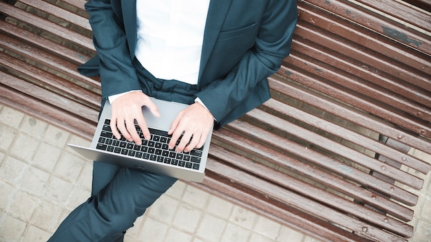 Una vista elevada de un hombre de negocios sentado en el banco usando una computadora portátil