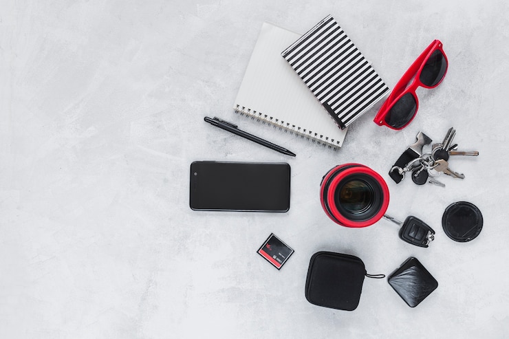 Foto gratuito vista elevada de la lente de la cámara, del cuaderno espiral, del teléfono móvil y de los accesorios personales en fondo