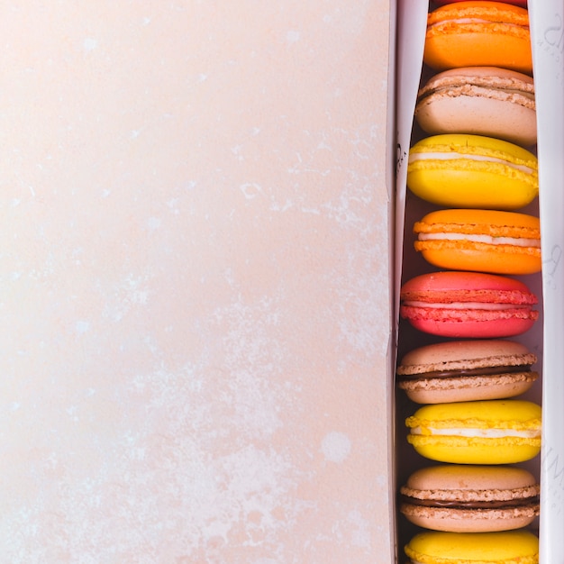 Foto gratuita una vista elevada de macarrones de colores en caja sobre fondo texturizado