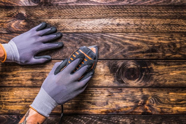 Vista elevada de la mano del carpintero que usa la máquina de lijado en fondo de madera