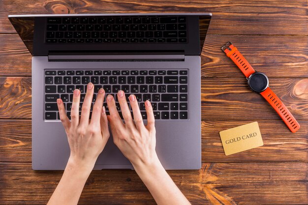 Vista elevada de la mano escribiendo en la computadora portátil sobre la mesa de madera