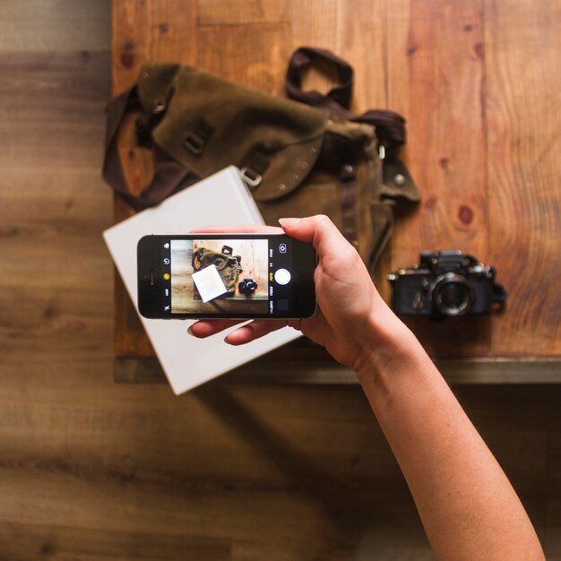 Vista elevada de la mano femenina tomando fotos de bolsa y cuaderno en la mesa