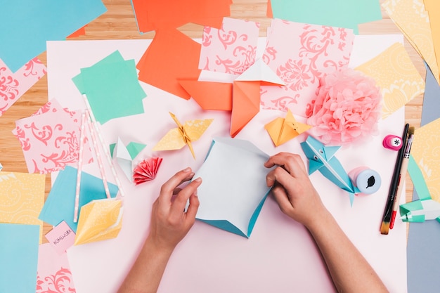 Vista elevada de la mano humana que hace el arte del papel del origami en la tabla de madera