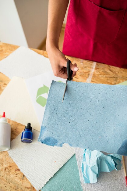 Vista elevada de mano de mujer cortando papel azul con tijeras