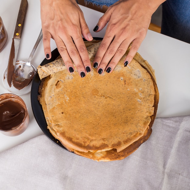 Foto gratuita una vista elevada de la mano de la mujer haciendo rodar el panqueque.