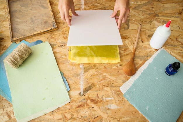 Vista elevada de la mano de la mujer que cubre la pulpa de papel sobre el escritorio de madera