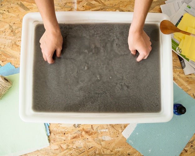 Vista elevada de la mano de una mujer que inserta el molde en la pulpa de papel