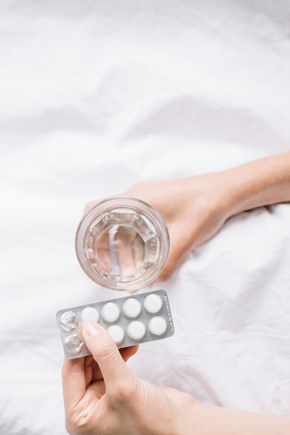 Vista elevada de la mano de la mujer con vaso de agua y pastillas