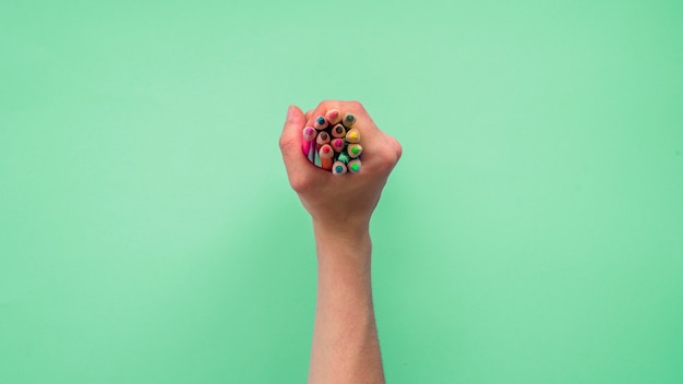 Foto gratuita vista elevada de la mano de una persona que sostiene un grupo de lápices de colores sobre fondo verde