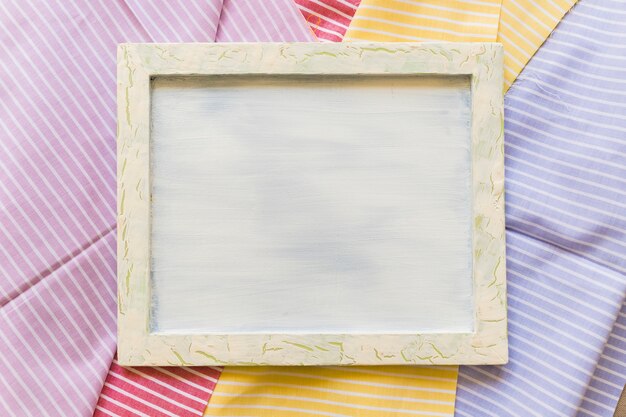 Vista elevada de un marco en blanco en textiles de patrones de rayas de colores