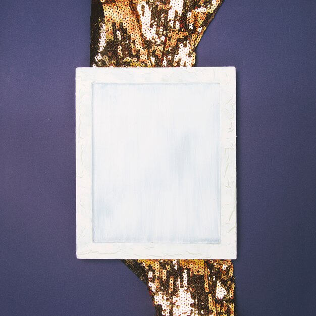 Vista elevada de un marco en blanco vacío en tela de lentejuelas dorada contra un fondo coloreado