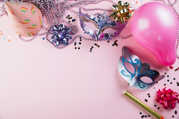Vista elevada de la máscara de carnaval de dos disfraces con material de decoración de fiesta sobre fondo rosa