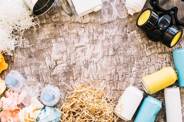 Vista elevada de la máscara de gas, latas, papel arrugado y botellas de plástico sobre fondo de madera