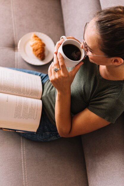 Una vista elevada de una mujer joven con un libro en su regazo tomando café