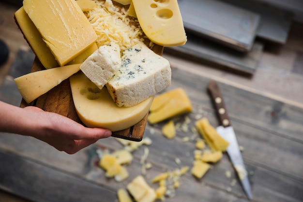 Foto gratuita una vista elevada de una mujer sosteniendo una bandeja de madera con queso fresco