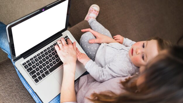 Vista elevada de la mujer con su hija usando la computadora portátil con pantalla blanca en blanco