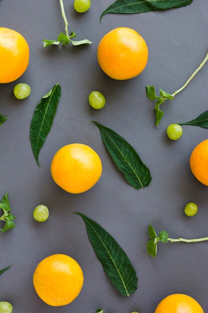 Una vista elevada de naranjas enteras; uvas; Hojas y ramitas sobre fondo gris.