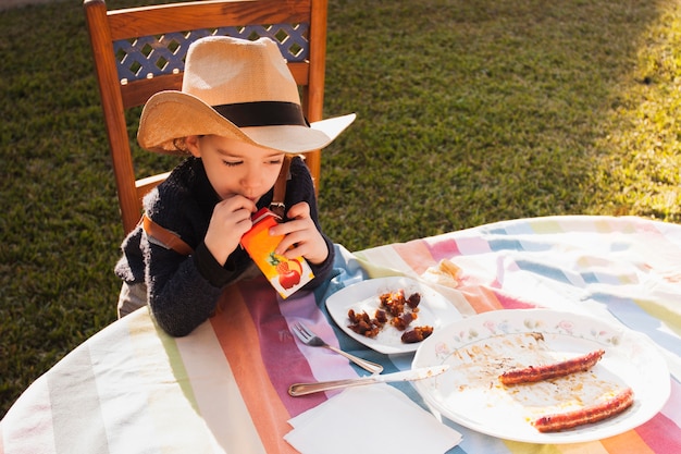 Foto gratuita vista elevada de una niña con sombrero bebiendo jugo