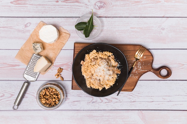 La vista elevada de nogal y la deliciosa pasta de fusilli trenzada adornan con queso rallado en superficie de madera